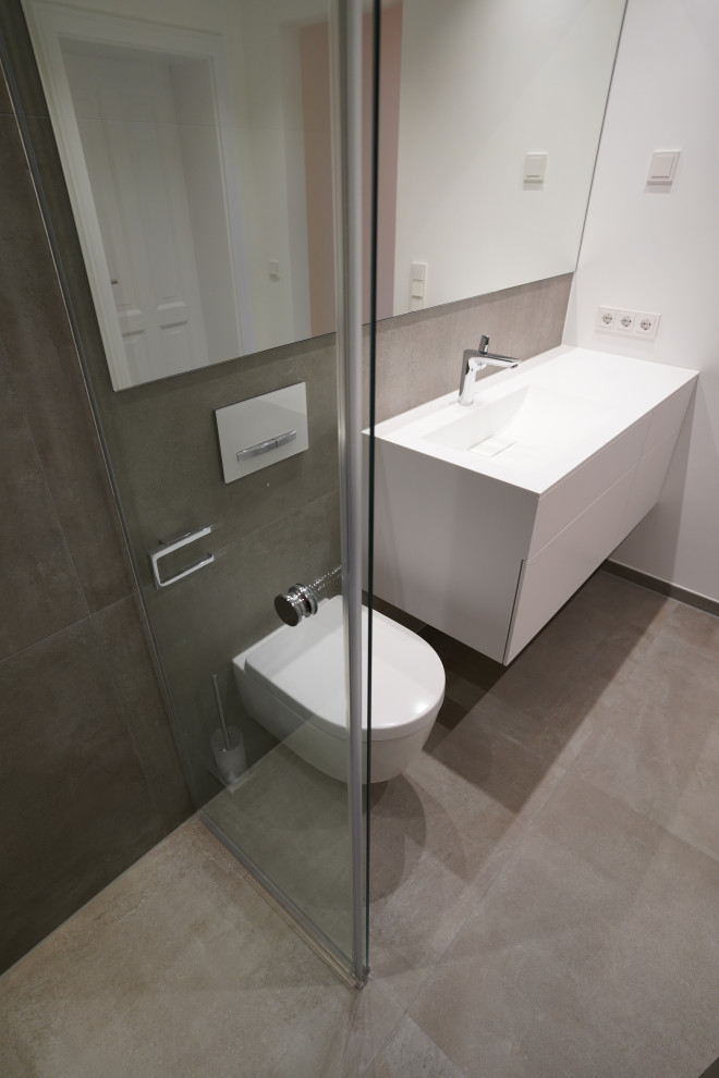 Huge minimalist 3/4 gray tile gray floor and single-sink bathroom photo in Munich with flat-panel cabinets, white cabinets, a wall-mount toilet, white walls, an integrated sink, solid surface countertops, white countertops and a floating vanity
