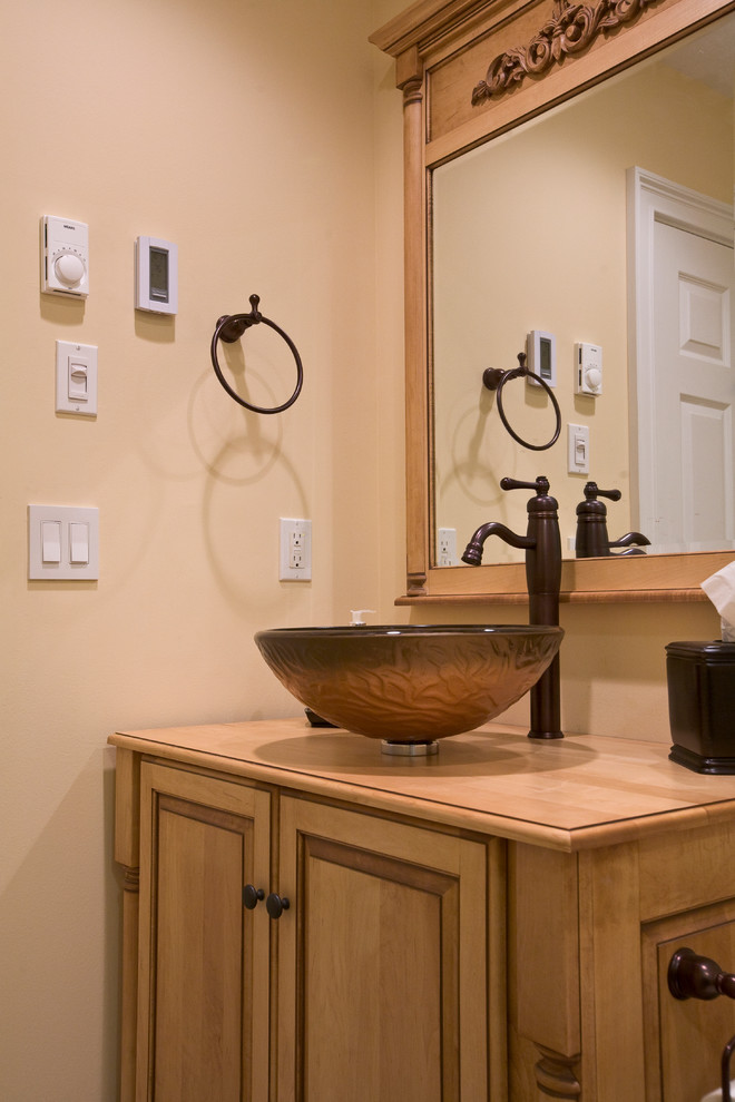 Photo of a small country 3/4 bathroom in New York with a vessel sink, furniture-like cabinets, light wood cabinets, wood benchtops, an alcove shower, a two-piece toilet, beige tile, porcelain tile, beige walls and porcelain floors.
