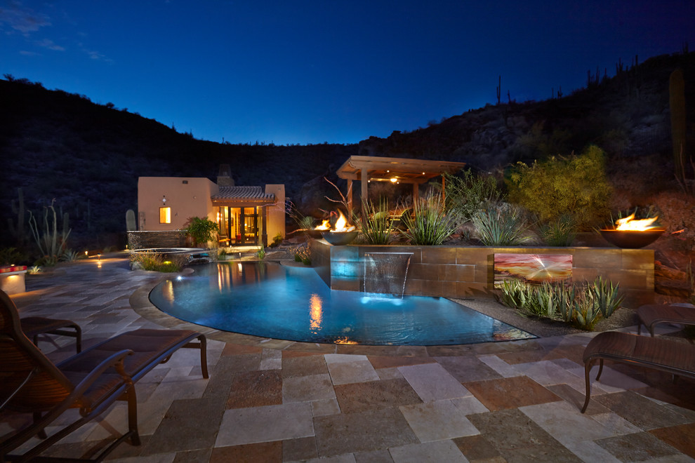 This is an example of an expansive backyard l-shaped infinity pool in Phoenix with a water feature and natural stone pavers.