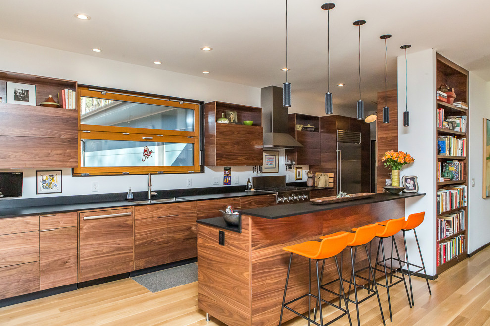 Inspiration for a large midcentury galley eat-in kitchen in Raleigh with an undermount sink, flat-panel cabinets, dark wood cabinets, laminate benchtops, black splashback, stainless steel appliances, medium hardwood floors, with island, brown floor and black benchtop.
