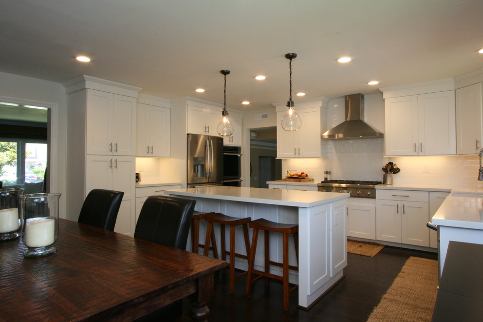 Large transitional u-shaped dark wood floor eat-in kitchen photo in Orange County with a farmhouse sink, shaker cabinets, white cabinets, quartz countertops, white backsplash, ceramic backsplash, stainless steel appliances and an island