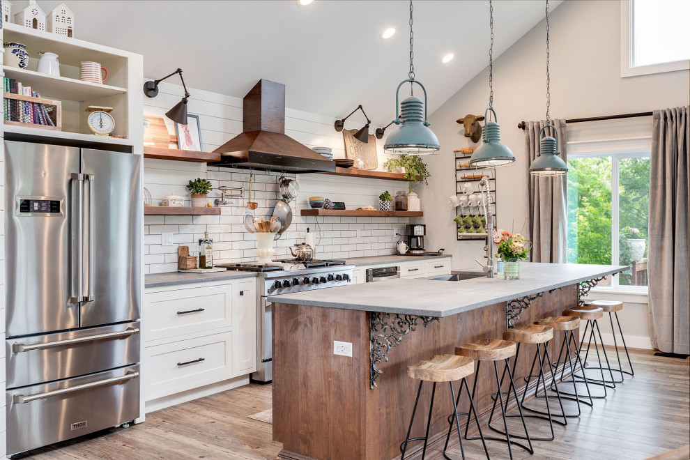 Farmhouse galley medium tone wood floor, brown floor and vaulted ceiling kitchen photo in Portland with a farmhouse sink, shaker cabinets, white cabinets, white backsplash, stainless steel appliances, an island and gray countertops