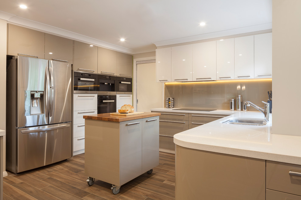 Expansive contemporary u-shaped eat-in kitchen in Sydney with an undermount sink, flat-panel cabinets, green cabinets, quartz benchtops, brown splashback, glass sheet splashback, stainless steel appliances, ceramic floors and multiple islands.