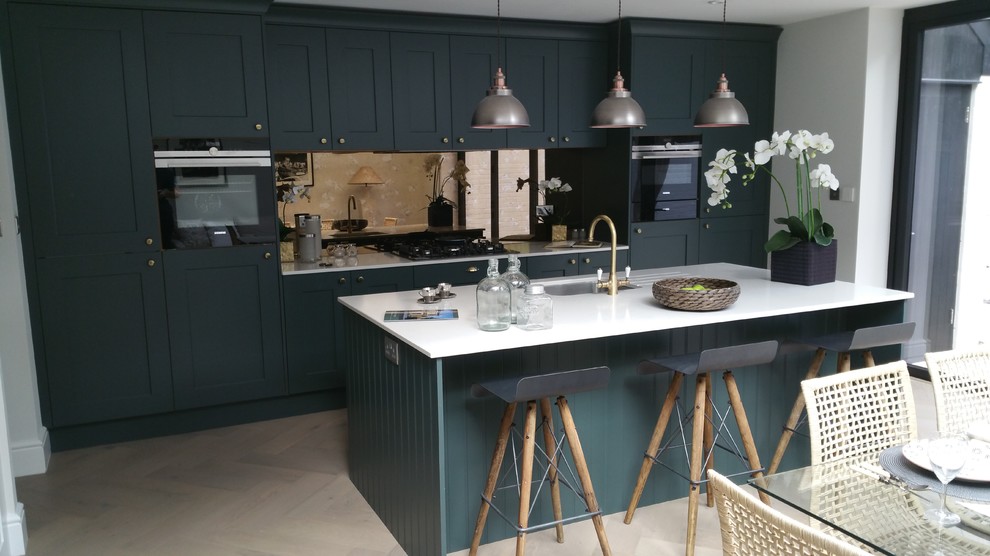 Inspiration for a mid-sized traditional single-wall eat-in kitchen in Berkshire with an undermount sink, shaker cabinets, green cabinets, quartzite benchtops, metallic splashback, glass sheet splashback, black appliances and with island.