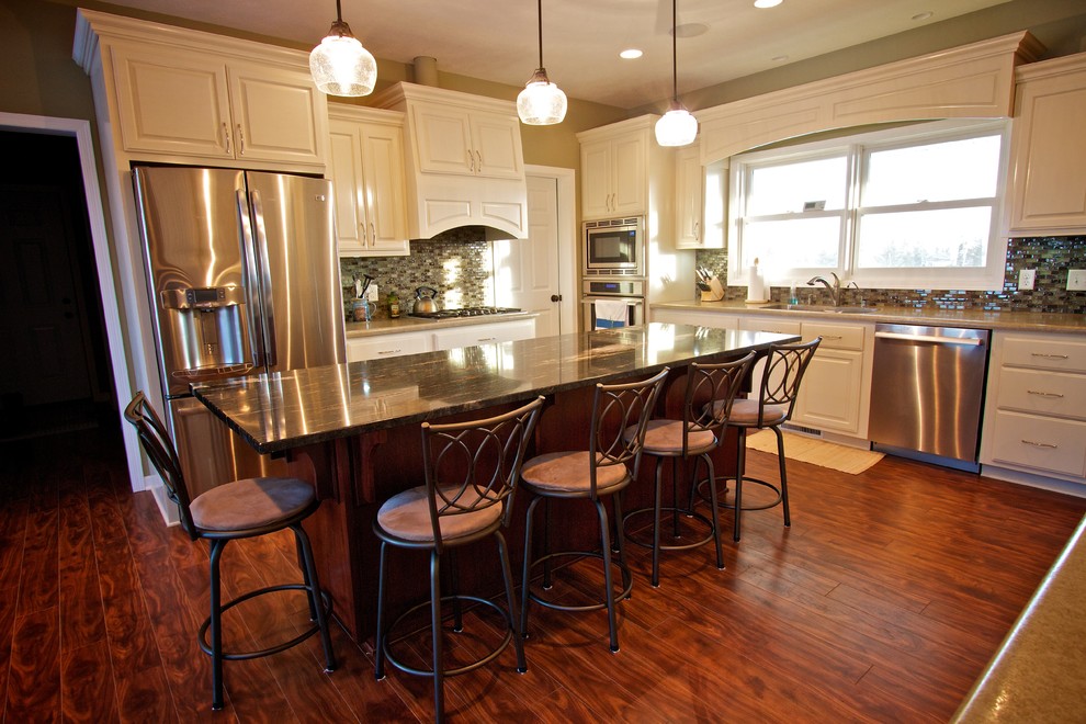 Example of a large u-shaped medium tone wood floor open concept kitchen design with a drop-in sink, raised-panel cabinets, white cabinets, multicolored backsplash, glass tile backsplash, stainless steel appliances and an island