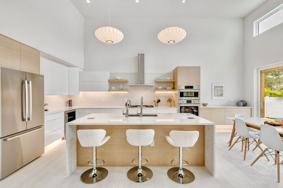 Photo of a mid-sized modern l-shaped open plan kitchen in Tampa with a single-bowl sink, flat-panel cabinets, light wood cabinets, quartz benchtops, white splashback, ceramic splashback, stainless steel appliances, light hardwood floors, with island, white floor and white benchtop.