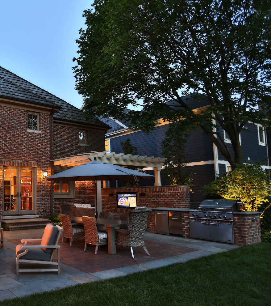 Aménagement d'une grande terrasse arrière classique avec une cuisine d'été, des pavés en pierre naturelle et une pergola.