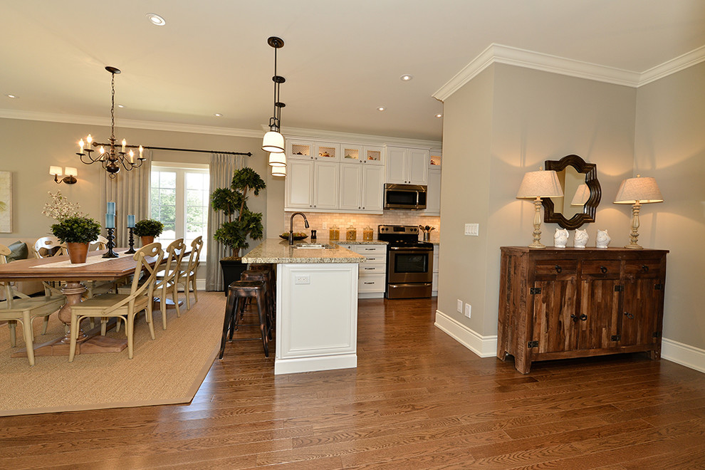Mid-sized transitional l-shaped medium tone wood floor eat-in kitchen photo in Toronto with a double-bowl sink, recessed-panel cabinets, white cabinets, granite countertops, beige backsplash, stone tile backsplash, stainless steel appliances and a peninsula