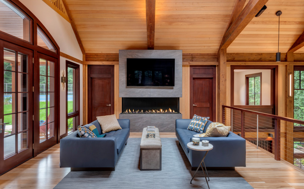 Inspiration for an expansive loft-style living room in Boston with light hardwood floors, a two-sided fireplace, a tile fireplace surround, a wall-mounted tv, brown floor, exposed beam and wood walls.