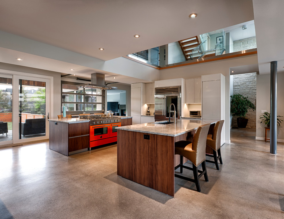 This is an example of a large contemporary eat-in kitchen in Calgary with a double-bowl sink, glass-front cabinets, medium wood cabinets, granite benchtops, orange splashback, coloured appliances, concrete floors and multiple islands.