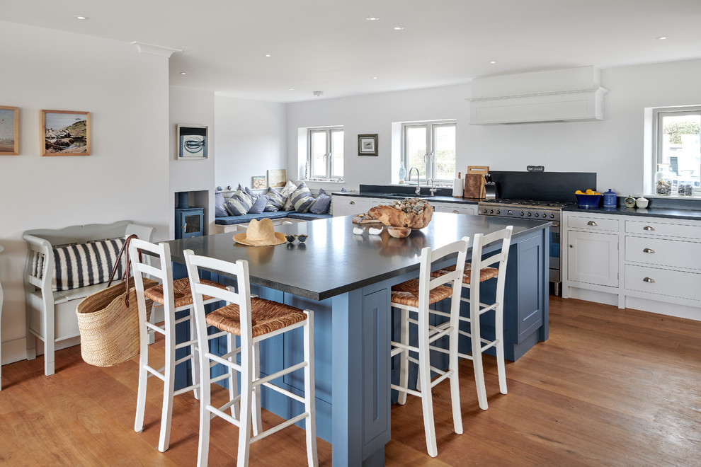 Mid-sized beach style l-shaped open plan kitchen in Hampshire with recessed-panel cabinets, blue cabinets, granite benchtops, medium hardwood floors, with island, brown floor and black benchtop.