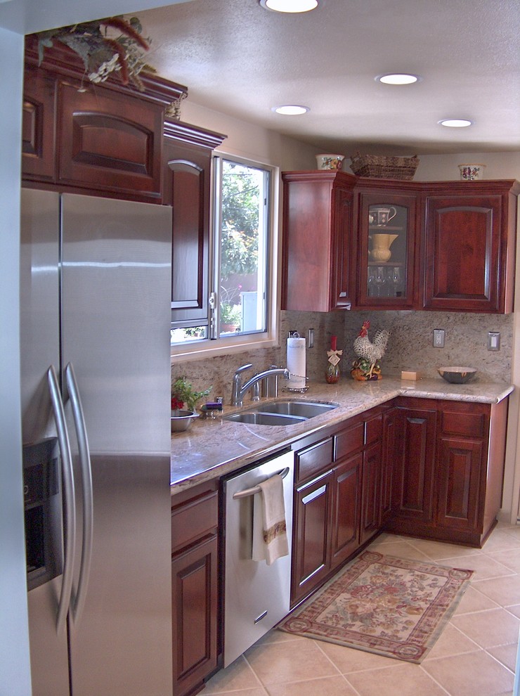 Inspiration for a small traditional galley kitchen in Orange County with a double-bowl sink, raised-panel cabinets, dark wood cabinets, granite benchtops, beige splashback, stone slab splashback, stainless steel appliances, ceramic floors and no island.