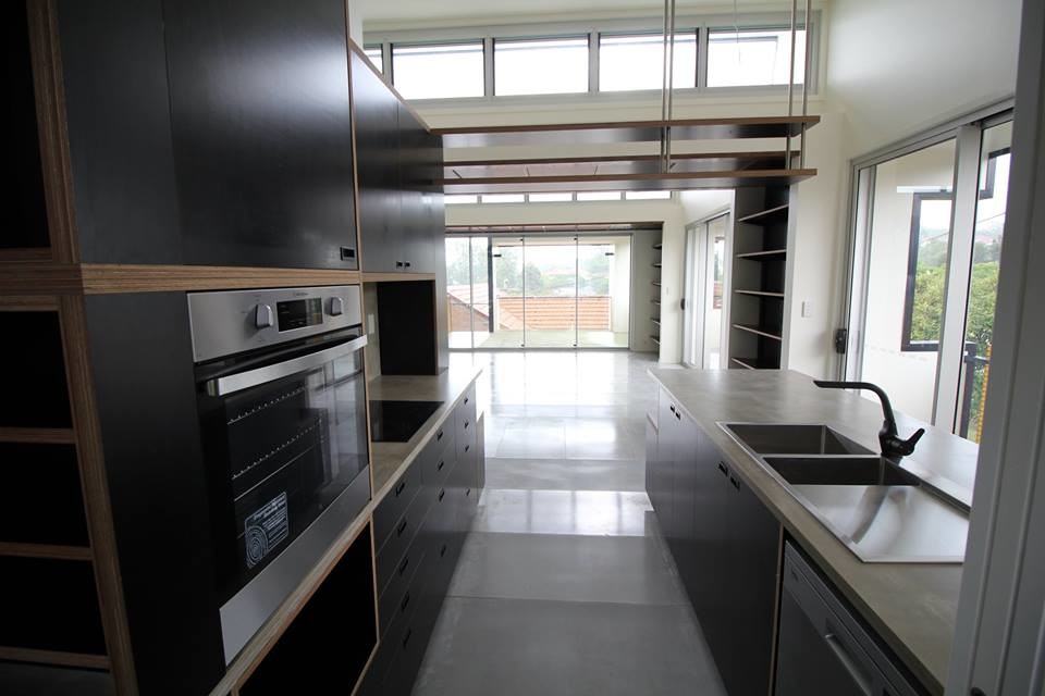 This is an example of a mid-sized industrial galley open plan kitchen in Other with black cabinets, with island, a double-bowl sink, flat-panel cabinets, concrete benchtops, grey splashback, stone slab splashback, stainless steel appliances and concrete floors.