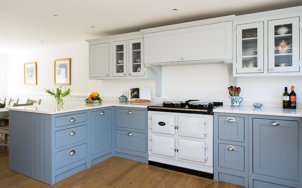 Mid-sized country eat-in kitchen in Gloucestershire with shaker cabinets, blue cabinets, light hardwood floors, no island and white appliances.