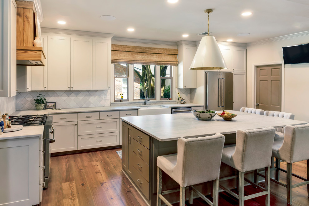 Inspiration for a mid-sized transitional l-shaped eat-in kitchen with a farmhouse sink, recessed-panel cabinets, beige cabinets, grey splashback, stainless steel appliances, with island, brown floor, grey benchtop and dark hardwood floors.