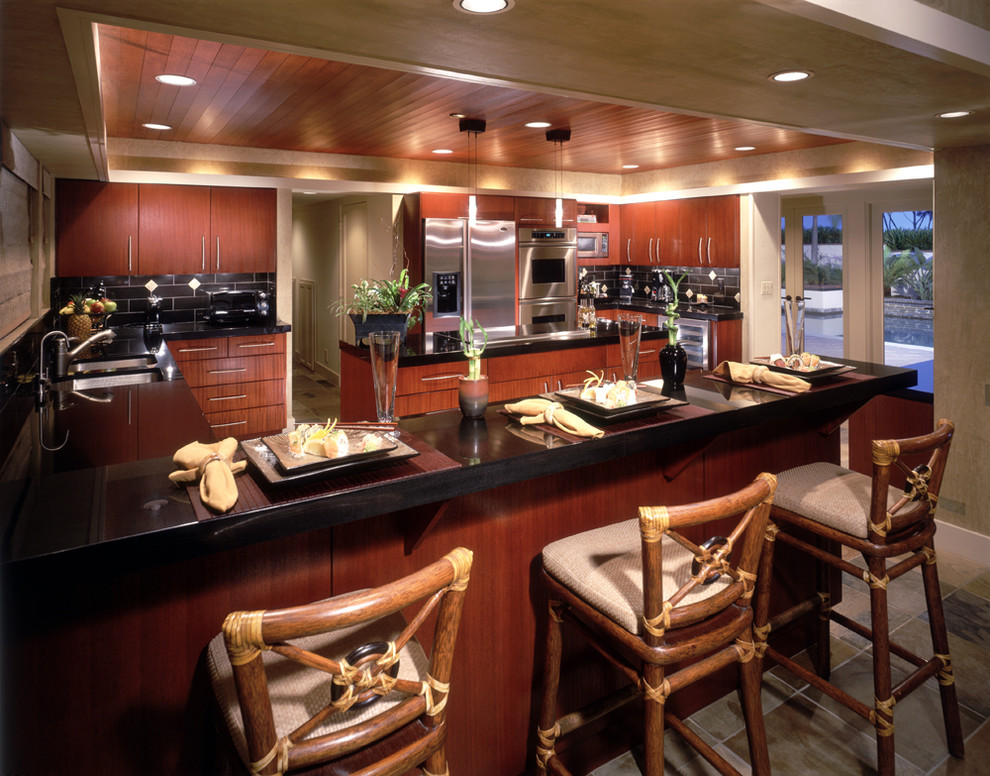 This is an example of a tropical kitchen in Orange County with flat-panel cabinets, dark wood cabinets, granite benchtops, black splashback, slate splashback and slate floors.