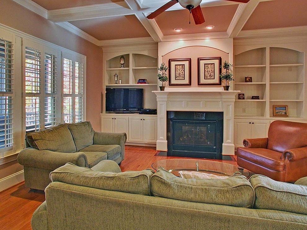 This is an example of a mid-sized traditional enclosed family room in Raleigh with beige walls, medium hardwood floors, a standard fireplace, a wood fireplace surround, a freestanding tv and pink floor.