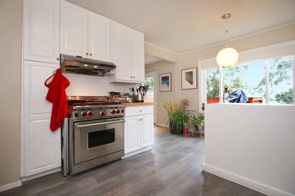 Photo of a mid-sized traditional kitchen in San Francisco with raised-panel cabinets, white cabinets, stainless steel appliances, porcelain floors, brown floor and wood benchtops.