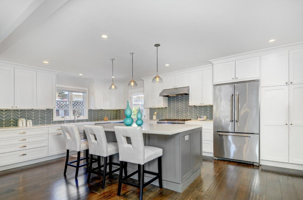 Example of a mid-sized transitional l-shaped dark wood floor and brown floor open concept kitchen design in San Francisco with shaker cabinets, white cabinets, blue backsplash, stainless steel appliances, an island, white countertops, an undermount sink, quartz countertops and glass tile backsplash