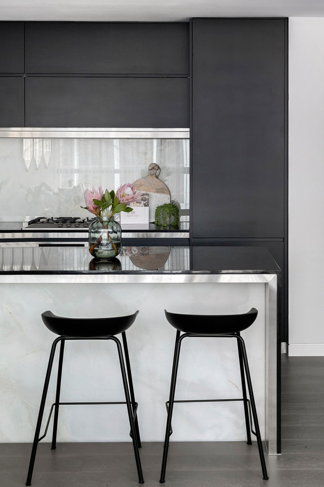 Photo of a contemporary kitchen in Sydney with flat-panel cabinets, black cabinets, stainless steel benchtops, white splashback, with island and brown floor.