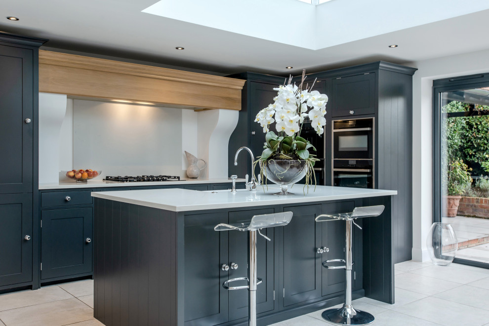 Design ideas for a mid-sized traditional open plan kitchen in Surrey with a single-bowl sink, shaker cabinets, blue cabinets, quartzite benchtops, white splashback, porcelain splashback, stainless steel appliances, ceramic floors, with island, grey floor and white benchtop.