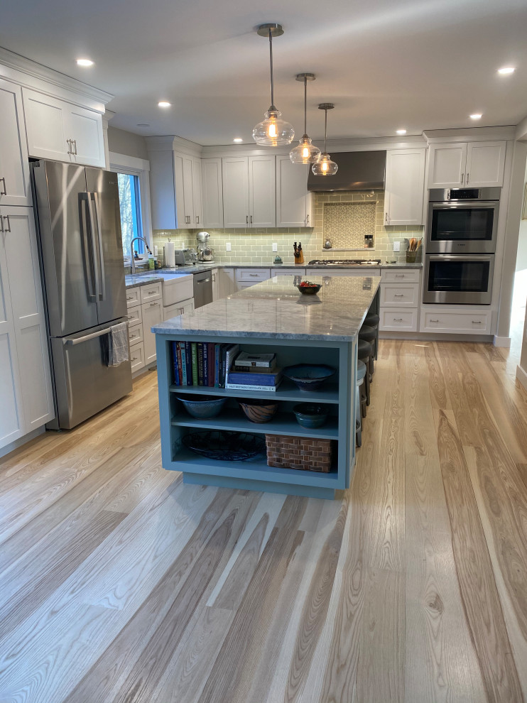 Photo of a mid-sized contemporary l-shaped eat-in kitchen in Portland Maine with a farmhouse sink, shaker cabinets, grey cabinets, quartz benchtops, green splashback, porcelain splashback, stainless steel appliances, medium hardwood floors, with island, white floor and grey benchtop.