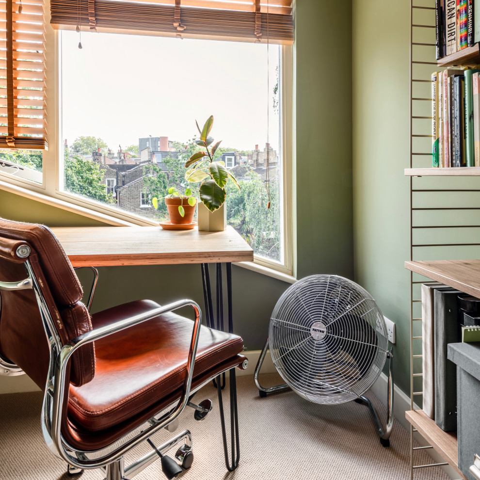 Bild på ett litet funkis hemmabibliotek, med gröna väggar, heltäckningsmatta, ett fristående skrivbord och beiget golv