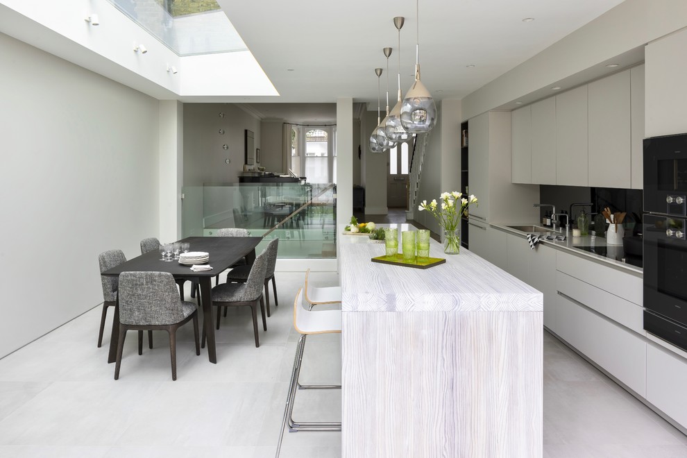Design ideas for an expansive contemporary galley open plan kitchen in London with an integrated sink, flat-panel cabinets, grey cabinets, wood benchtops, grey splashback, mirror splashback, panelled appliances, ceramic floors, with island, grey floor and grey benchtop.