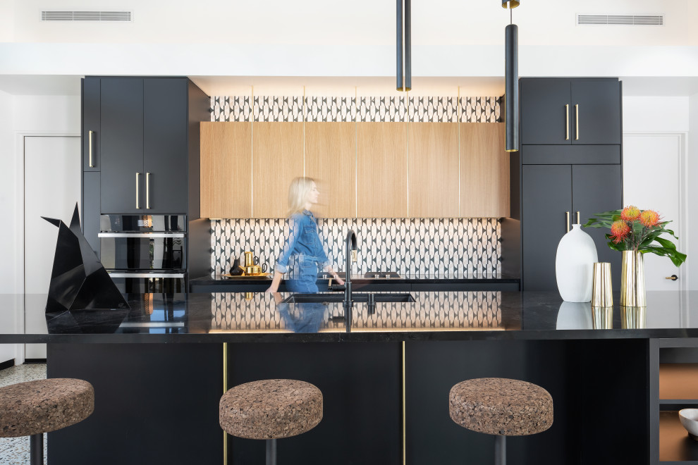 Photo of a large midcentury single-wall kitchen/diner in Los Angeles with flat-panel cabinets, black cabinets, multi-coloured splashback, stone tiled splashback, black appliances, terrazzo flooring, an island and black worktops.