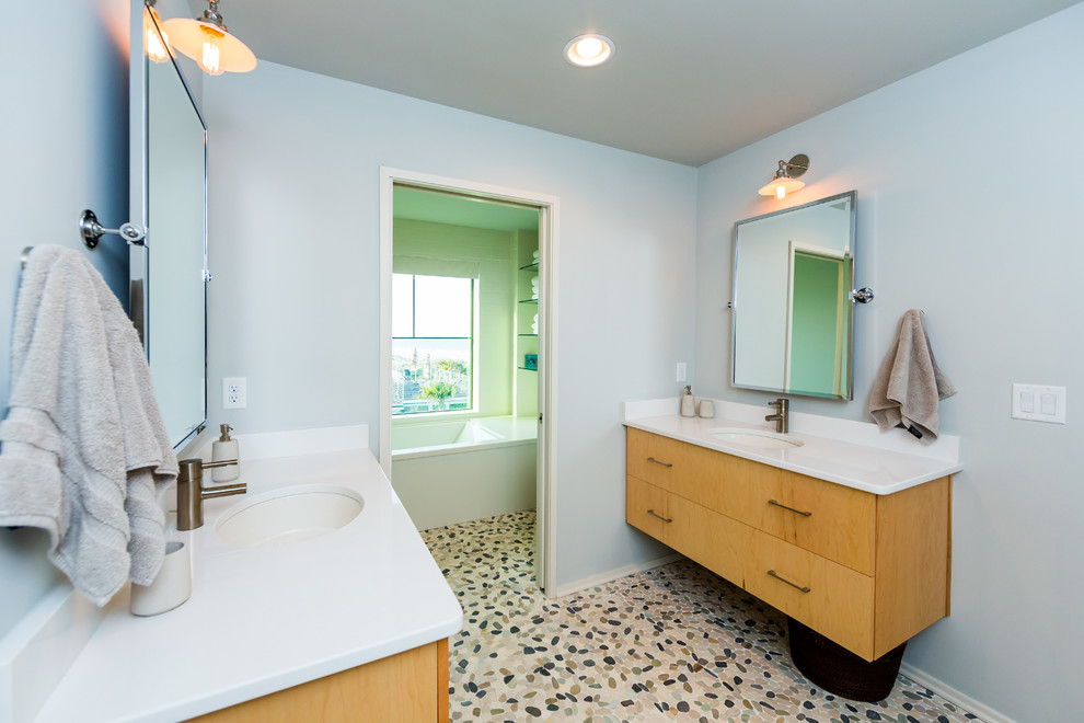 Mid-sized beach style bathroom in Jacksonville with an undermount sink, flat-panel cabinets, light wood cabinets, engineered quartz benchtops, an undermount tub, a shower/bathtub combo, a two-piece toilet, porcelain tile, grey walls and pebble tile floors.