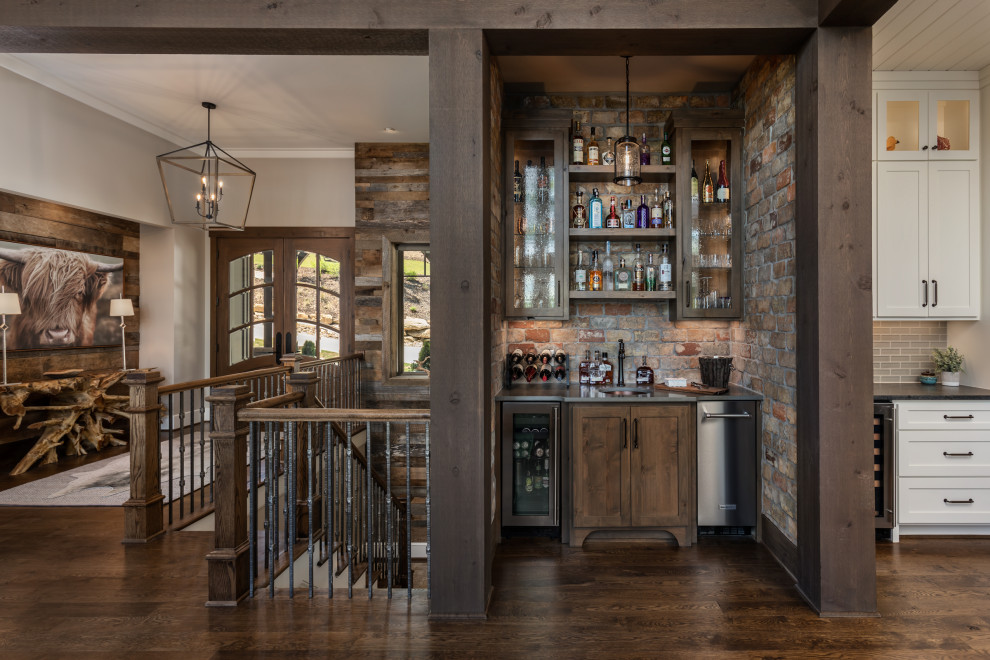 Inspiration for a large country single-wall home bar in Other with an undermount sink, shaker cabinets, brown floor, black benchtop, dark wood cabinets, brown splashback, brick splashback and dark hardwood floors.