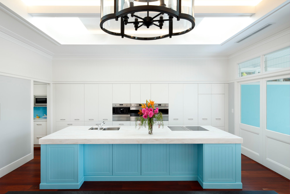 Inspiration for a large transitional galley open plan kitchen in Sydney with an undermount sink, recessed-panel cabinets, blue cabinets, blue splashback, glass sheet splashback, stainless steel appliances, dark hardwood floors, with island, red floor and white benchtop.