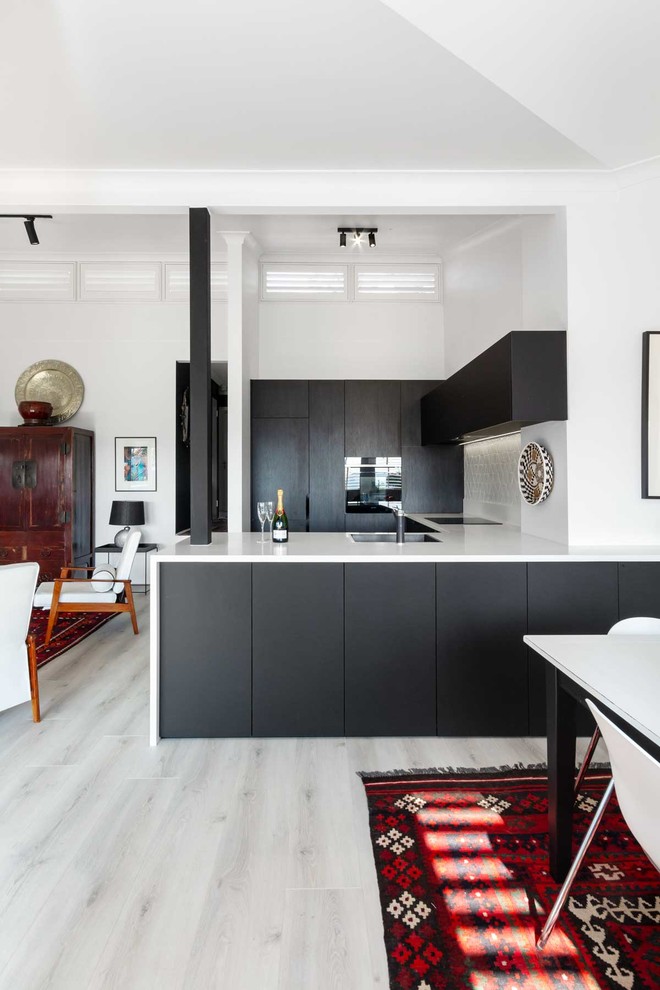 Small eclectic u-shaped eat-in kitchen in Sydney with a single-bowl sink, black cabinets, solid surface benchtops, white splashback, mosaic tile splashback, black appliances, laminate floors, grey floor and white benchtop.