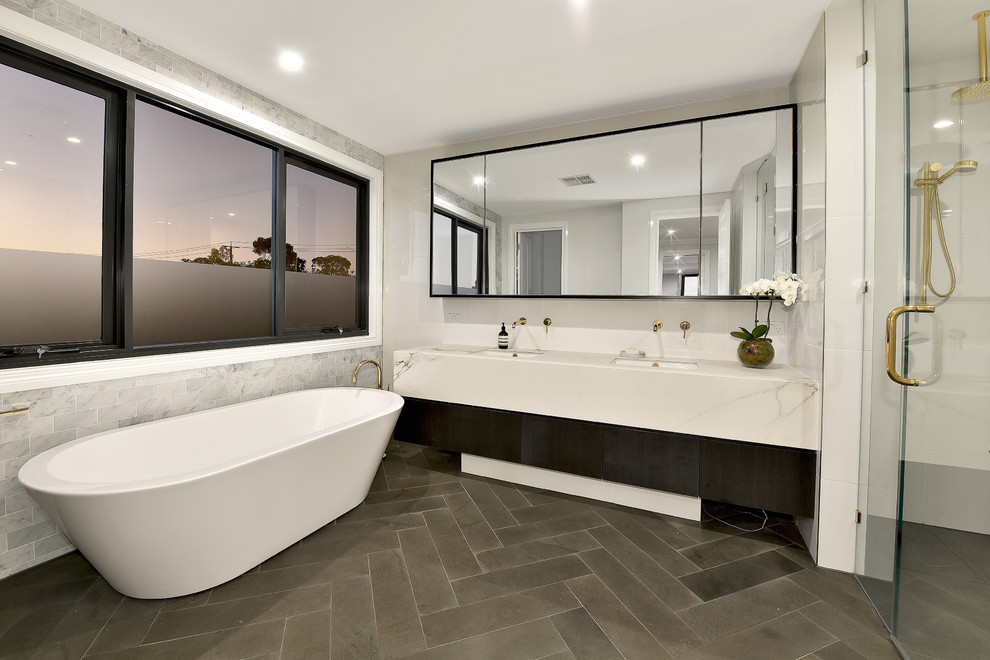 This is an example of a mid-sized contemporary master bathroom in Melbourne with dark wood cabinets, a freestanding tub, a double shower, white tile, ceramic tile, grey walls, ceramic floors, an undermount sink, engineered quartz benchtops, grey floor, a hinged shower door and grey benchtops.