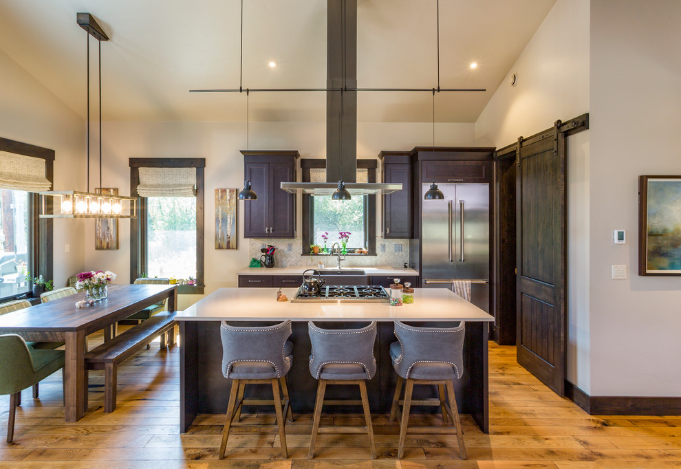 Design ideas for a country galley eat-in kitchen in Denver with a farmhouse sink, dark wood cabinets, quartz benchtops, stone tile splashback, stainless steel appliances, medium hardwood floors, with island, white benchtop, grey splashback and brown floor.