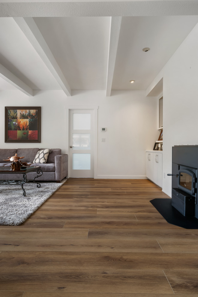 This is an example of a medium sized beach style formal open plan living room in Seattle with white walls, vinyl flooring, a wood burning stove, a metal fireplace surround, brown floors and a coffered ceiling.