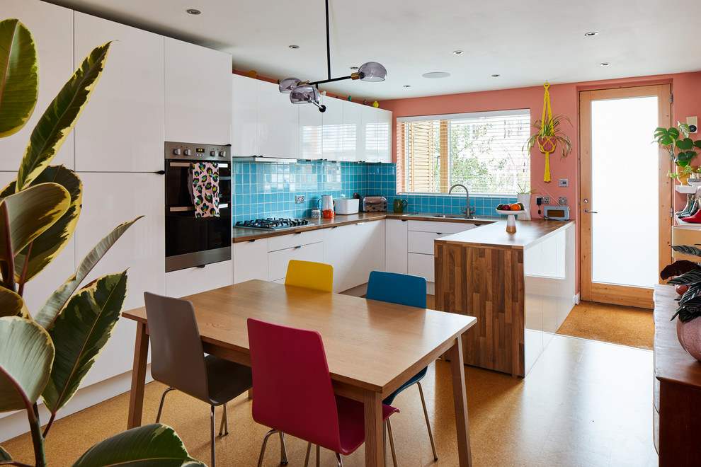 Inspiration for a midcentury u-shaped eat-in kitchen in London with a single-bowl sink, flat-panel cabinets, white cabinets, wood benchtops, blue splashback, cork floors and a peninsula.