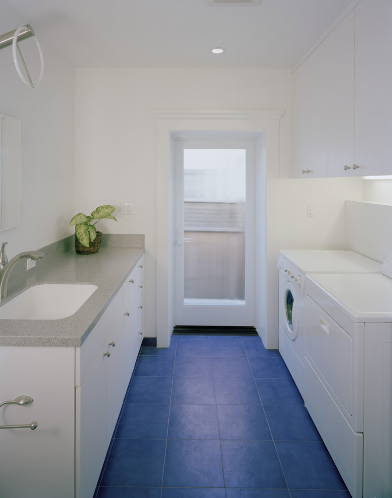 Inspiration for a large modern galley utility room in San Francisco with an undermount sink, flat-panel cabinets, white cabinets, solid surface benchtops, white walls, ceramic floors, a side-by-side washer and dryer and blue floor.