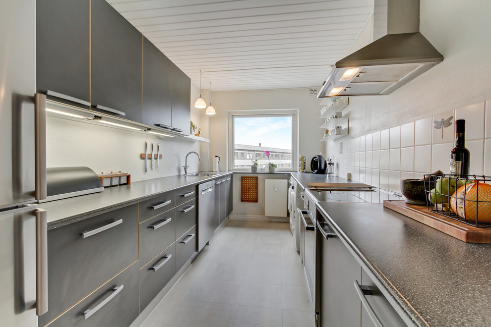 Design ideas for a mid-sized contemporary galley separate kitchen in Aalborg with a drop-in sink, flat-panel cabinets, white splashback, stainless steel appliances, no island, grey cabinets, laminate benchtops, stone tile splashback and ceramic floors.