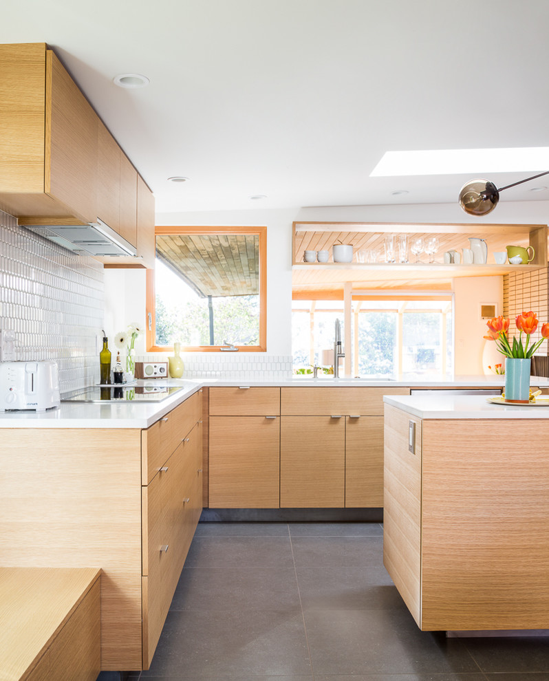 This is an example of a mid-sized midcentury l-shaped eat-in kitchen in Seattle with an undermount sink, flat-panel cabinets, light wood cabinets, quartz benchtops, white splashback, glass tile splashback, stainless steel appliances and with island.