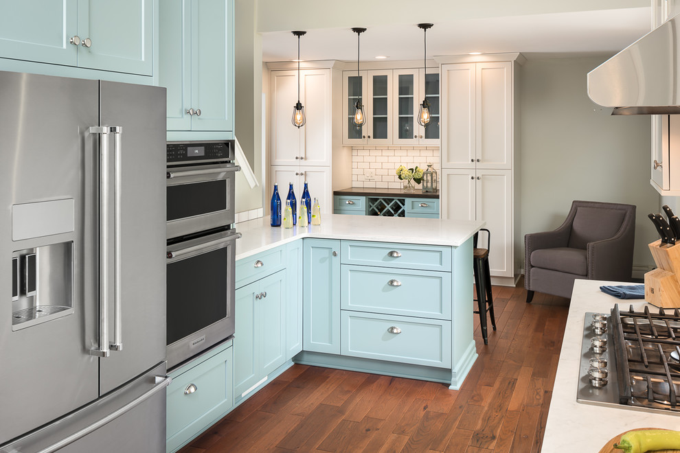 Example of a large transitional l-shaped medium tone wood floor kitchen design in New York with an undermount sink, flat-panel cabinets, blue cabinets, quartz countertops, white backsplash, ceramic backsplash, stainless steel appliances and a peninsula