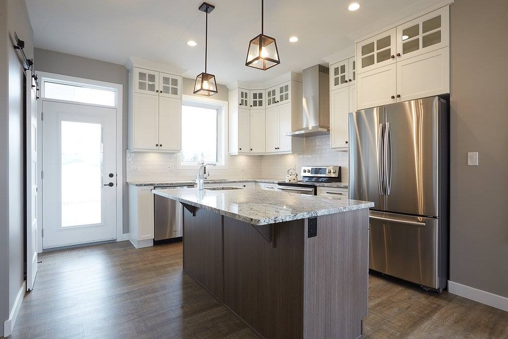 Mid-sized transitional l-shaped dark wood floor and brown floor kitchen photo with an undermount sink, shaker cabinets, white cabinets, granite countertops, white backsplash, subway tile backsplash, stainless steel appliances and an island