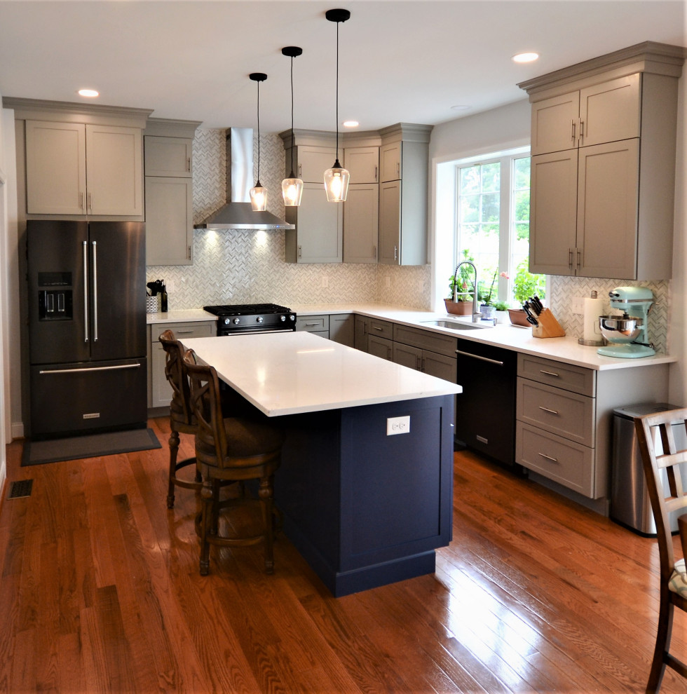 This is an example of a large transitional l-shaped eat-in kitchen in Philadelphia with an undermount sink, flat-panel cabinets, blue cabinets, quartz benchtops, white splashback, ceramic splashback, black appliances, medium hardwood floors, with island, brown floor and white benchtop.