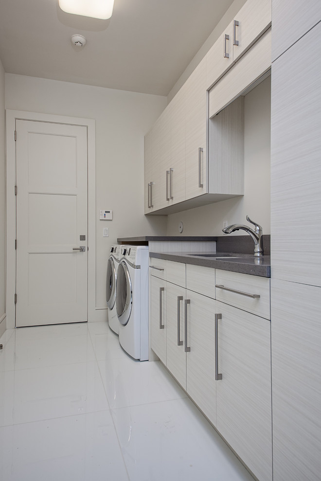 Design ideas for a mid-sized modern single-wall utility room in Miami with an undermount sink, flat-panel cabinets, white walls, a side-by-side washer and dryer, white floor, grey benchtop and grey cabinets.