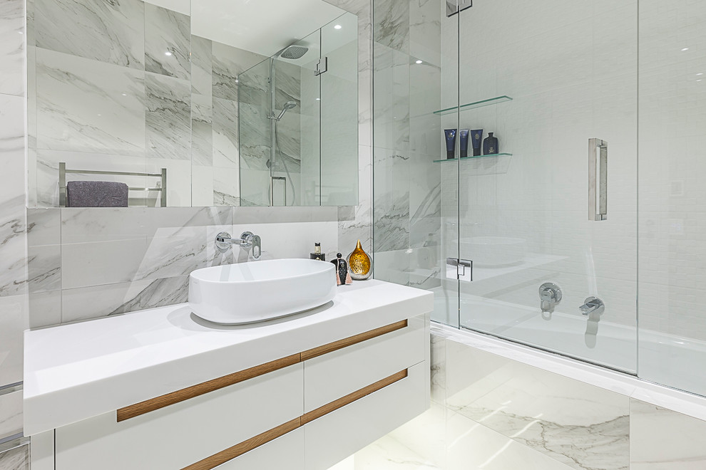 Mid-sized contemporary master bathroom in Auckland with an alcove tub, a shower/bathtub combo, a one-piece toilet, a vessel sink, a hinged shower door, flat-panel cabinets, white cabinets, marble floors and solid surface benchtops.
