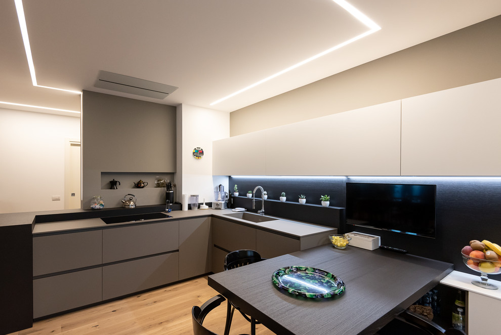 Design ideas for a contemporary l-shaped eat-in kitchen in Venice with a single-bowl sink, flat-panel cabinets, grey cabinets, black splashback, light hardwood floors and grey benchtop.