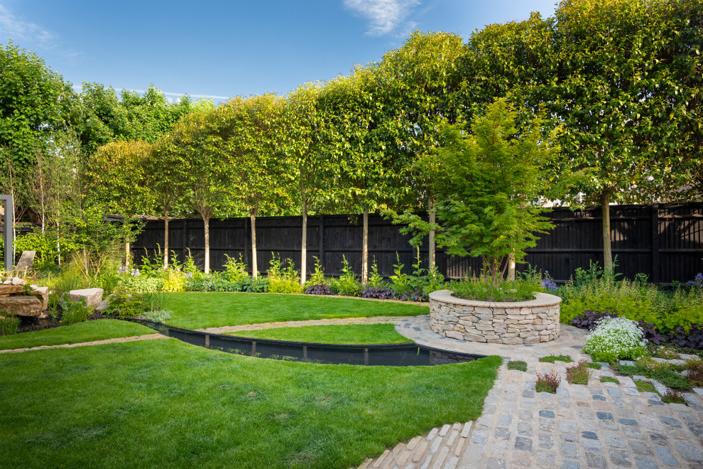 Photo of a contemporary back garden for summer in London with a waterfall, natural stone paving and a wood fence.