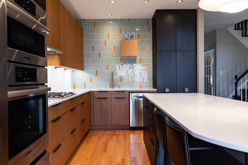 This is an example of a mid-sized contemporary l-shaped open plan kitchen in Philadelphia with an undermount sink, flat-panel cabinets, brown cabinets, quartz benchtops, white splashback, porcelain splashback, stainless steel appliances, light hardwood floors, with island, brown floor and white benchtop.