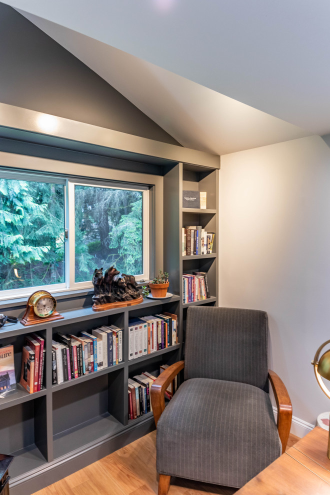 This is an example of a mid-sized contemporary home office in Seattle with a library, grey walls, light hardwood floors, a wood stove, a metal fireplace surround, a freestanding desk and brown floor.
