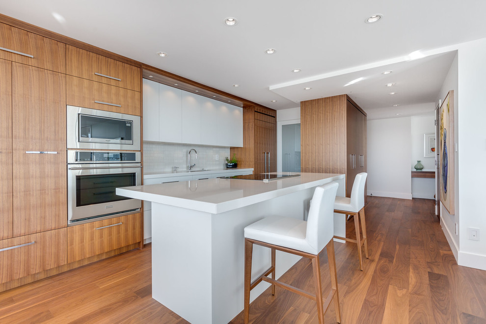 Open concept kitchen - mid-sized transitional galley medium tone wood floor open concept kitchen idea in Vancouver with an undermount sink, flat-panel cabinets, medium tone wood cabinets, quartz countertops, white backsplash, ceramic backsplash, stainless steel appliances and an island